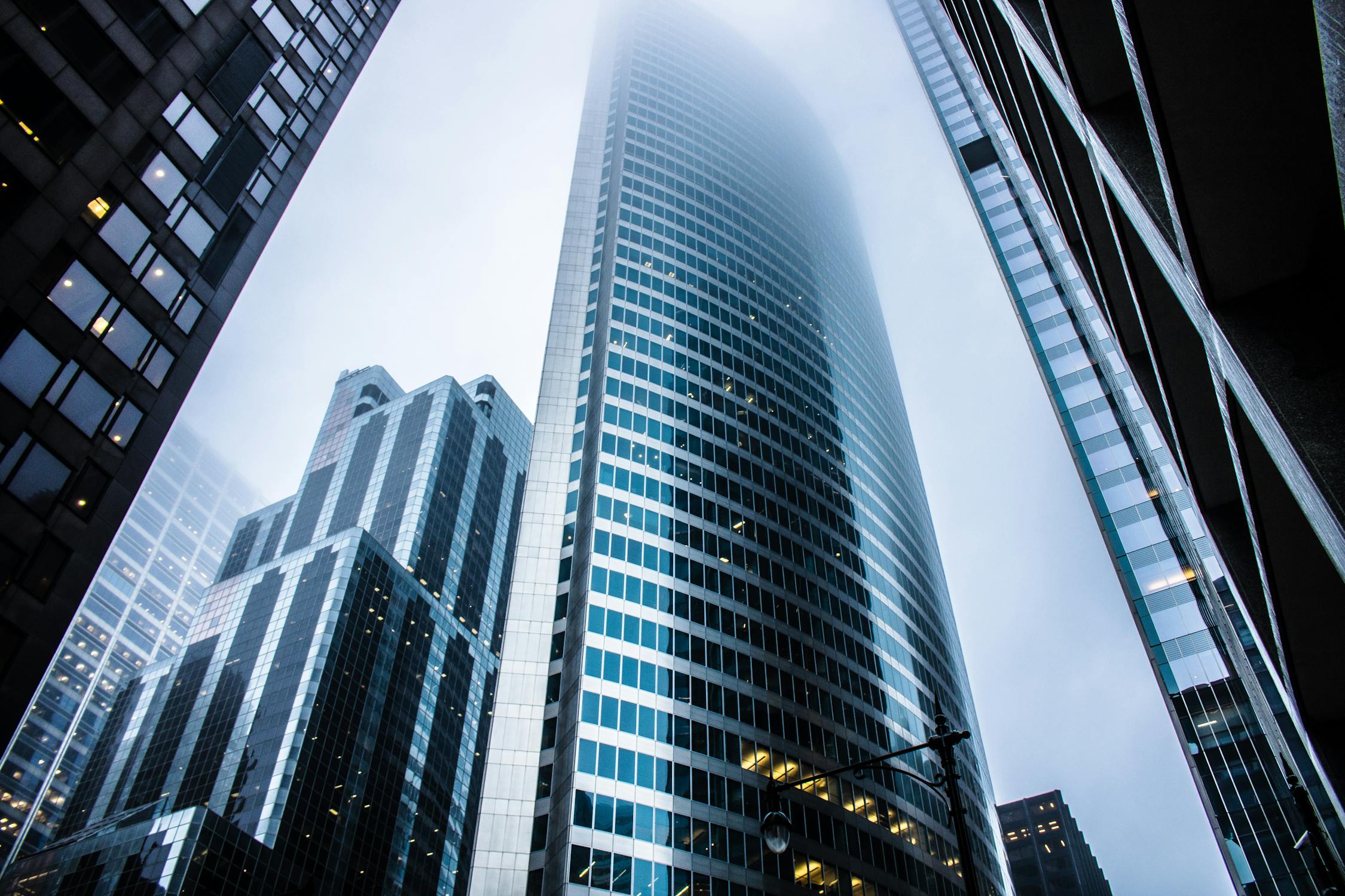 A modern office space with floor-to-ceiling windows providing ample natural light. The room features stylish furniture, including ergonomic chairs and a sleek wooden table, creating a professional and inviting atmosphere. A city skyline is visible through the large windows.